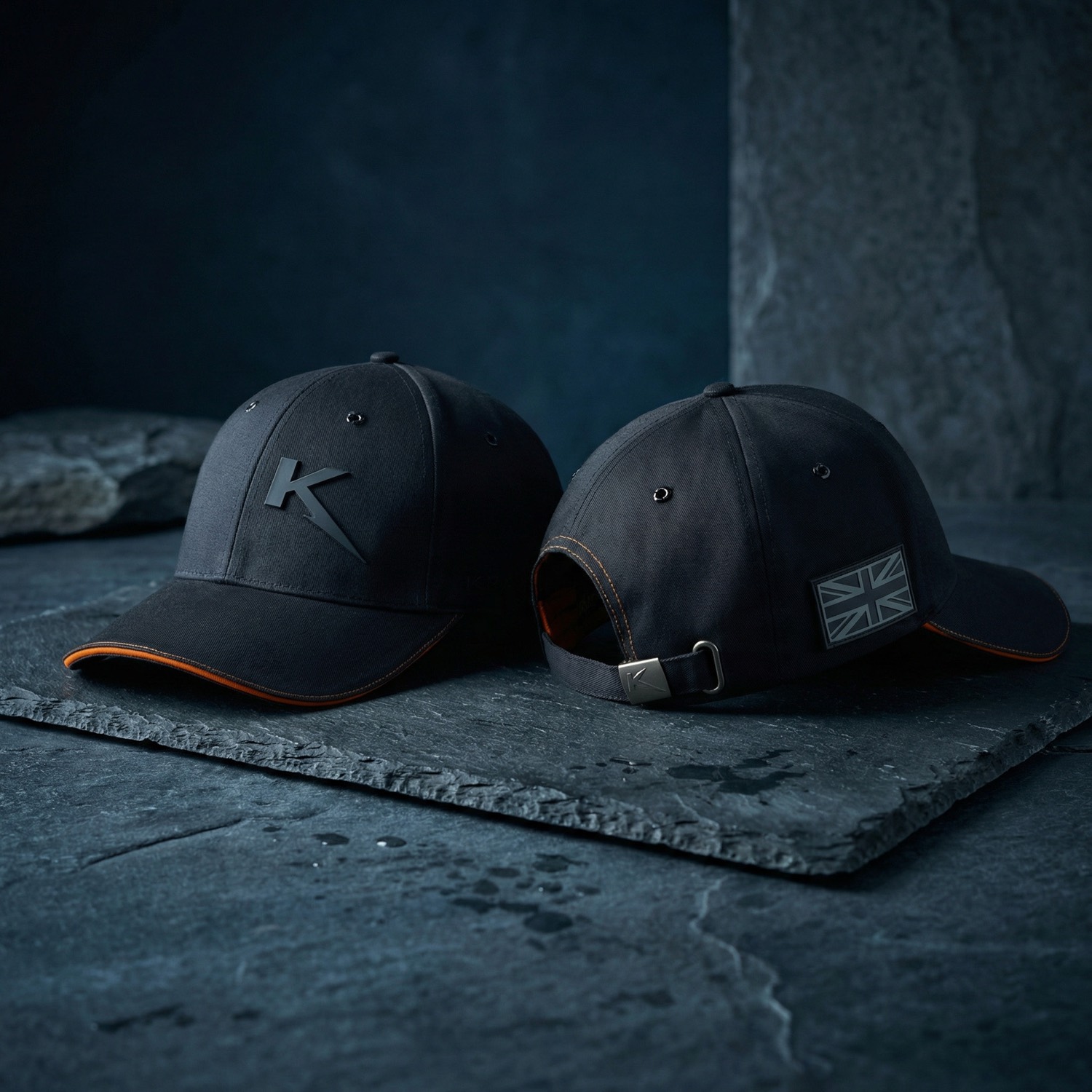 Two custom black caps with debossed monogram and Union flag patch, shot on slate